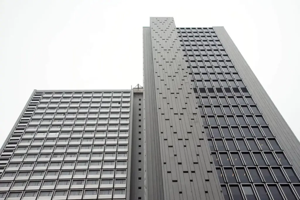 Close‑up perspectief van een moderne hoogbouwtoren met strakke, geometrische gevels en repetitieve ramen.