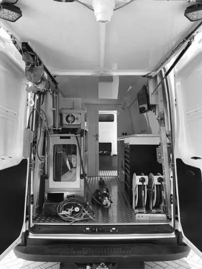 Binnenkant van een inspectie‑ en renovatievoertuig met freesrobot, bedieningsunit, kabelhaspels en technische apparatuur voor rioolinspectie, reiniging en sleufloze renovatiewerken.