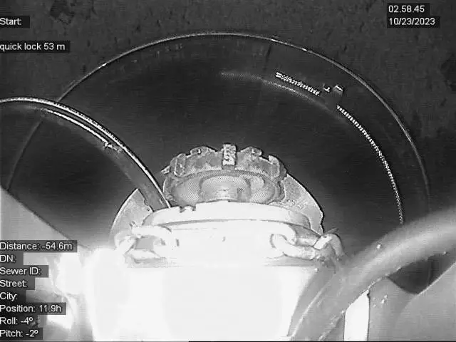 Camerabeeld van een QuickLock‑herstellingsmodule binnenin een rioolleiding, met zicht op de mechanische expansieringen en overlay‑gegevens over afstand, positie en inspectieparameters tijdens een rioolinspectie.