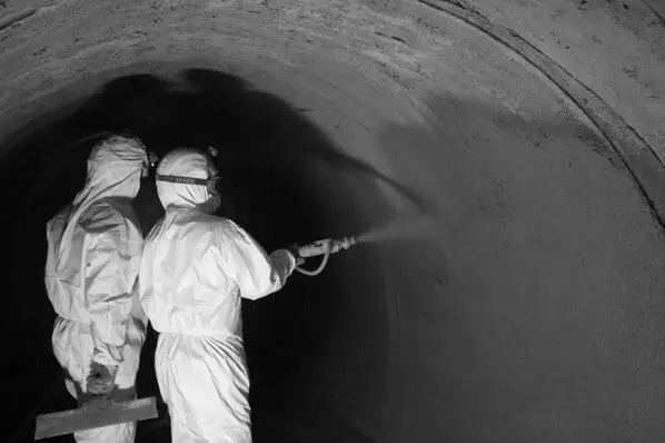Spuitbetonwerk in een ondergrondse tunnel, waarbij twee medewerkers in beschermende pakken de tunnelwand behandelen met een spuitlans als onderdeel van structurele renovatiewerken.